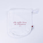 Pochon de naissance en gaze de coton blanc brodé rose J1 sur fond blanc épuré.