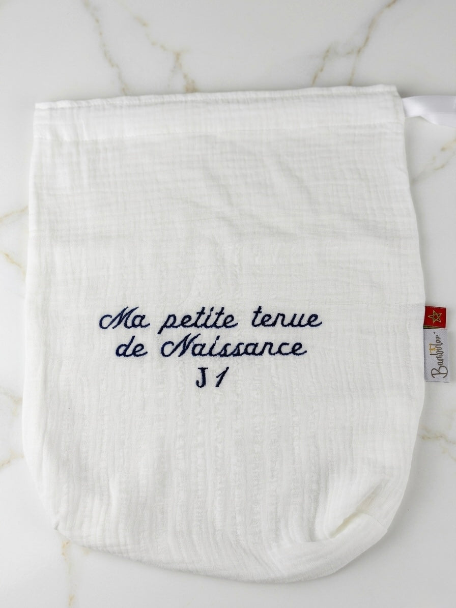 Pochette naissance J1 en gaze de coton blanche sur marbre, broderie bleue.