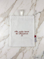 Pochon de naissance blanc brodé terracotta J1 posé sur un plan de travail en marbre blanc et doré.